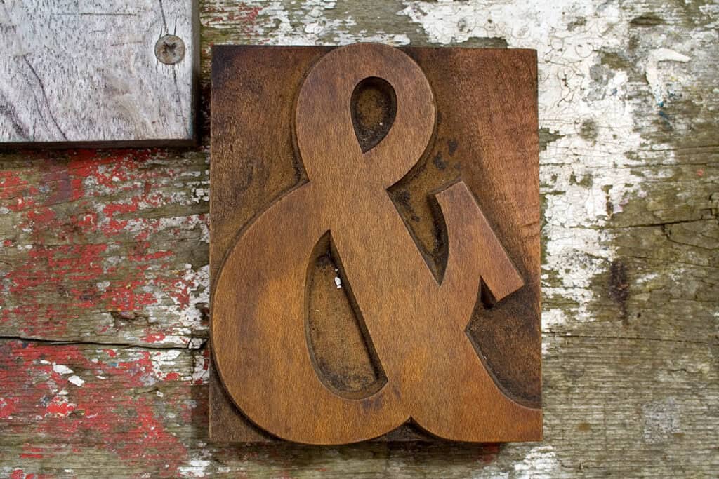 Ampersand carved into a wood block, on weathered wood surface.